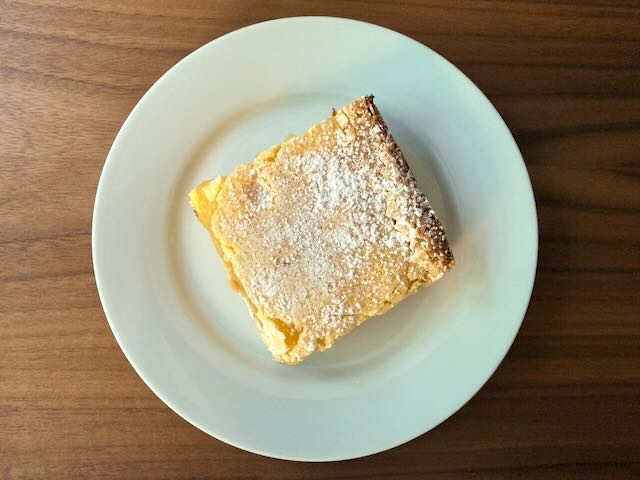 Golden vanilla custard slice dusted with powdered sugar on a white plate